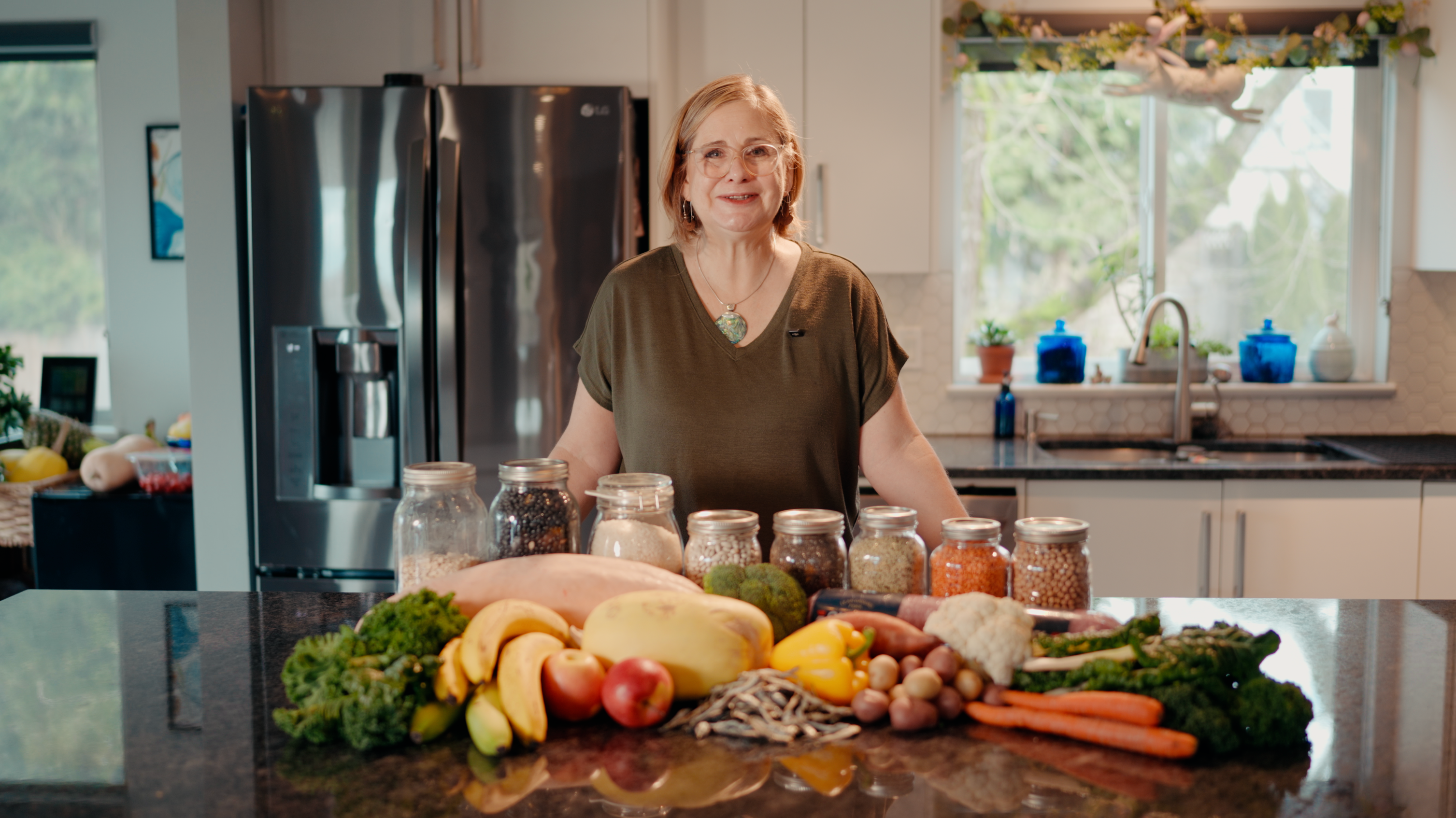 Course instructor standing at a kitchen counter surrounded by fresh produce and mason jars of whole ingredients