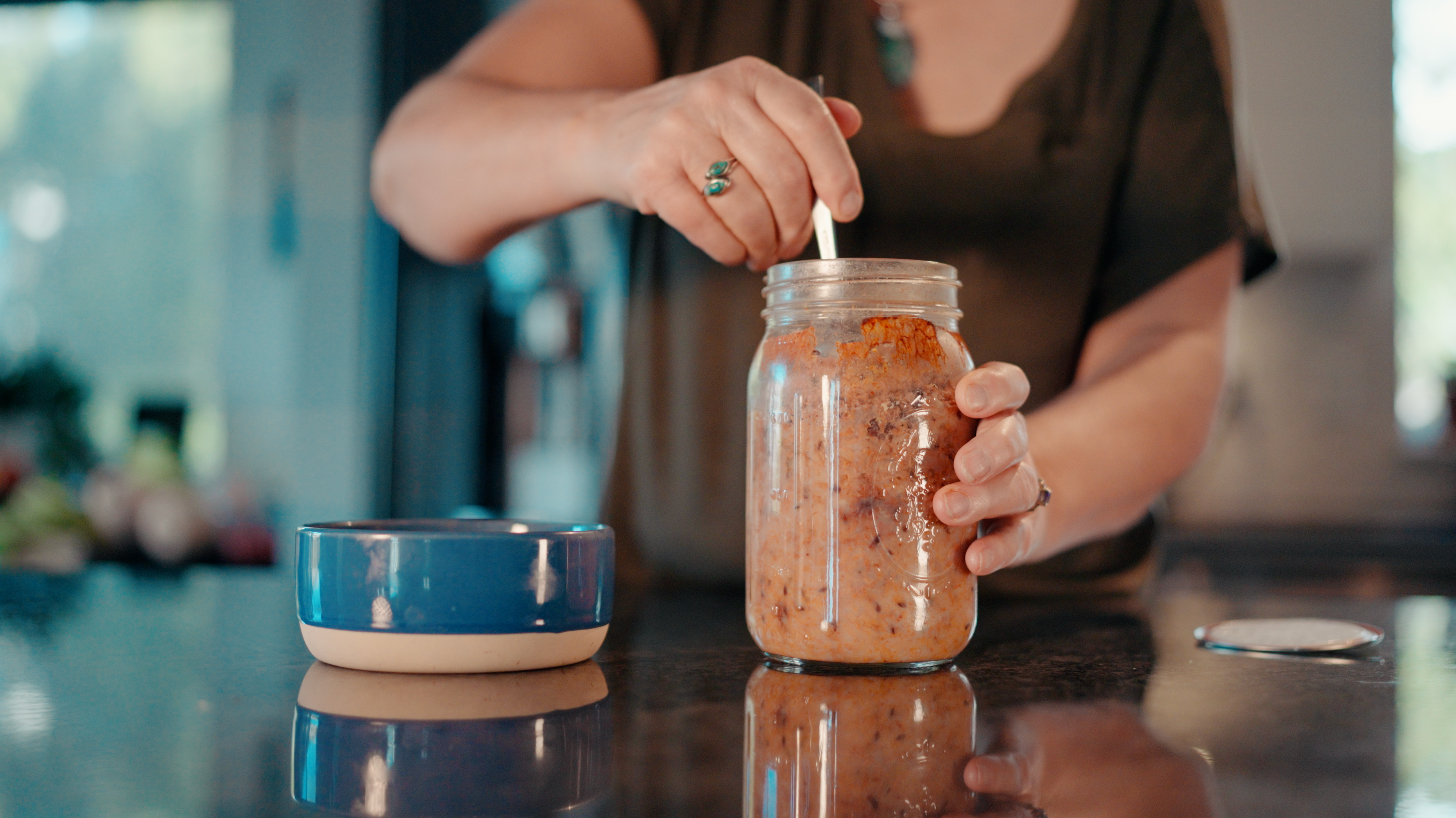 Hands stirring homemade dog food in a mason jar beside a blue ceramic dog bowl